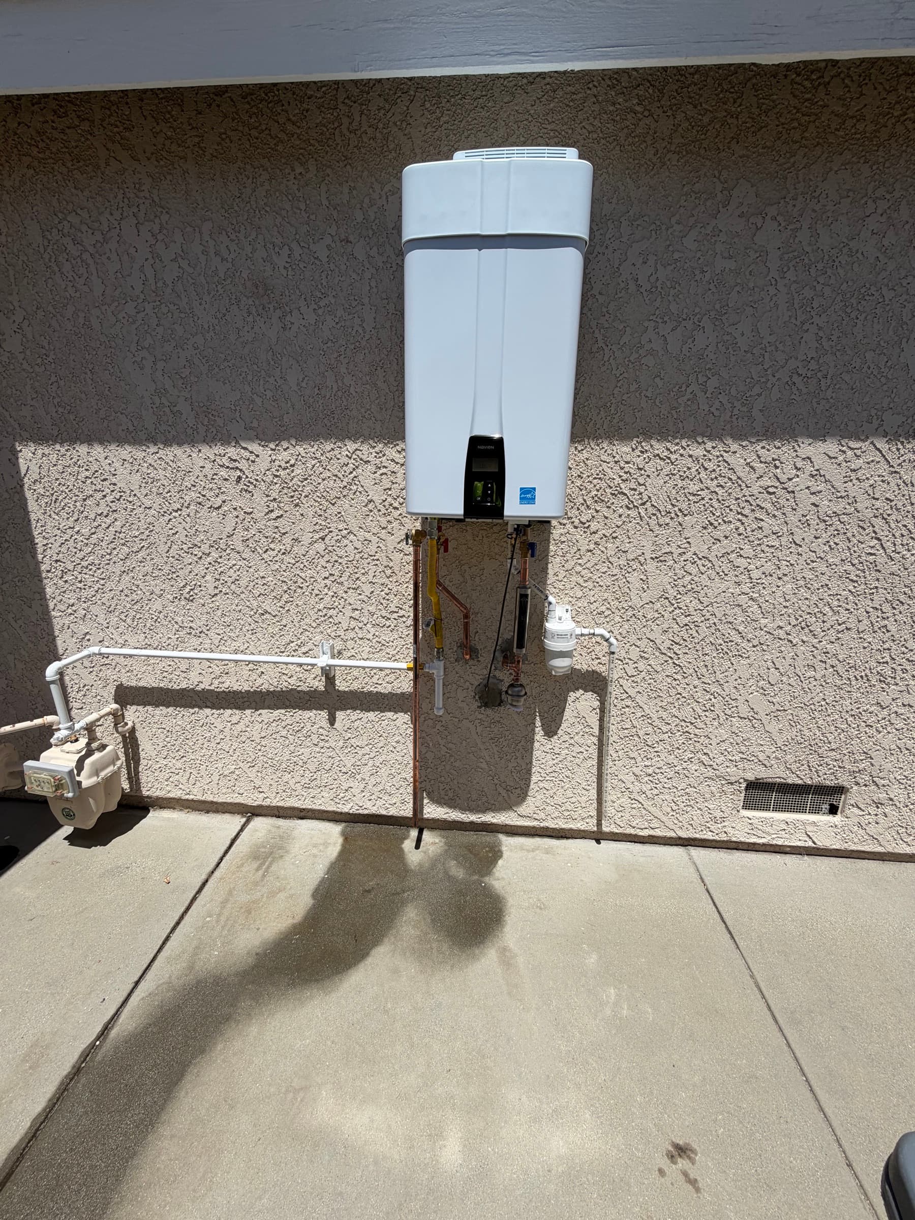 Navien tankless water heater mounted on an exterior stucco wall with copper supply lines, a gas line, and a scale filter, installed after the original tank unit flooded the garage